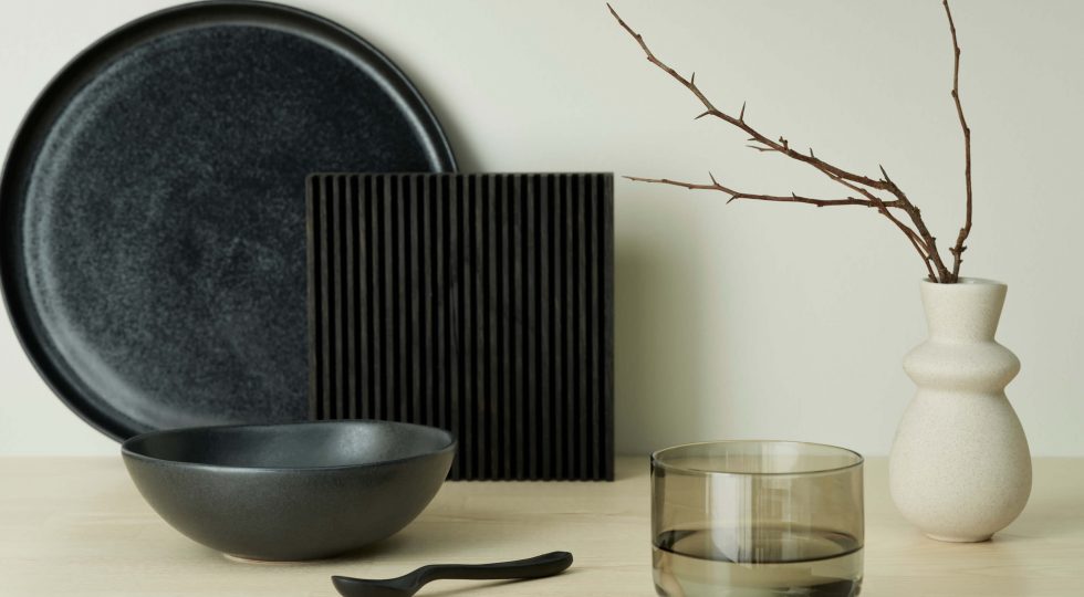 Svart keramik och vit vas med kvist på en bänkskiva i ask